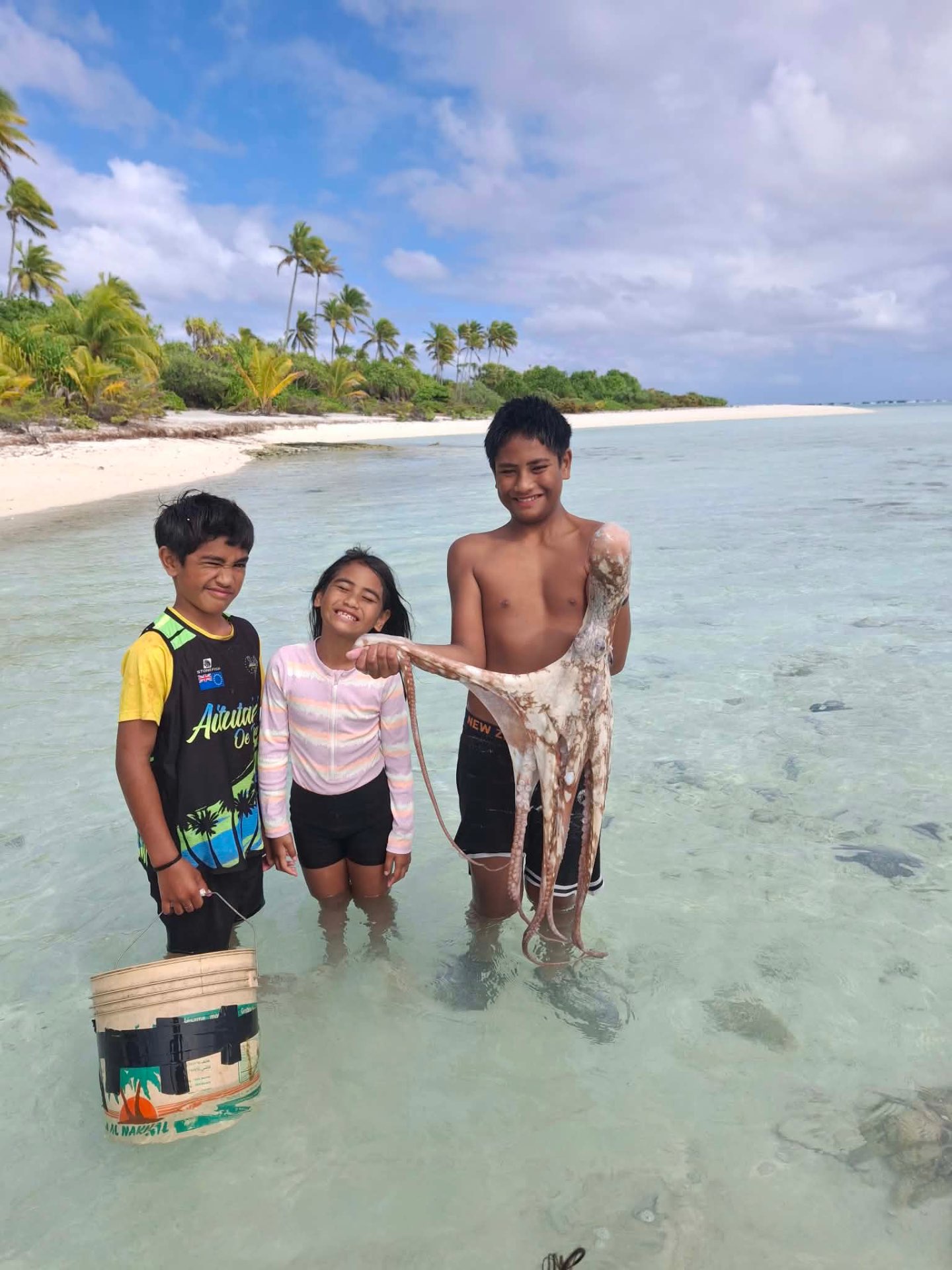 Three children holding an octopus in the shallow Aitutaki lagoon